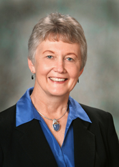Photo of Marilyn Rothert has short grey hair and smiles kindly at the camera on a portrait backdrop.
