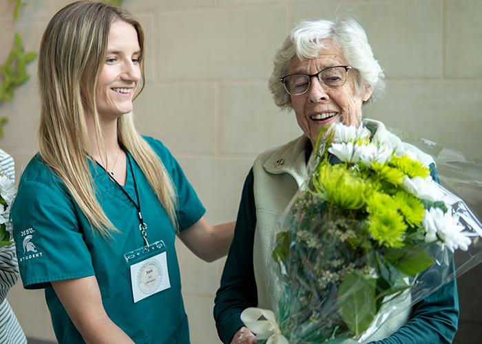 A College of Nursing student hands over a flower bouquet to a College of Nursing alumna, Millie Heslip. Millie was in the first CON graduating class from 1954.