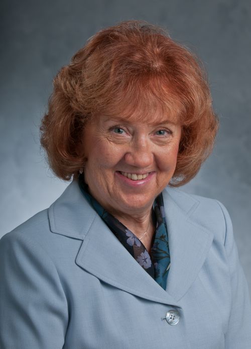 Photo of Mildred Horodynski smiling at camera with bright red hair and blue eyes on a portrait backdrop.